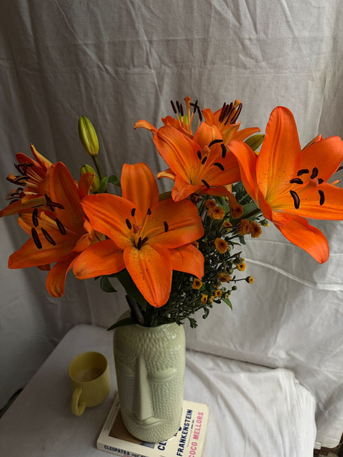 Orange lilies in bloom with unopened lily buds arranged in a vase
